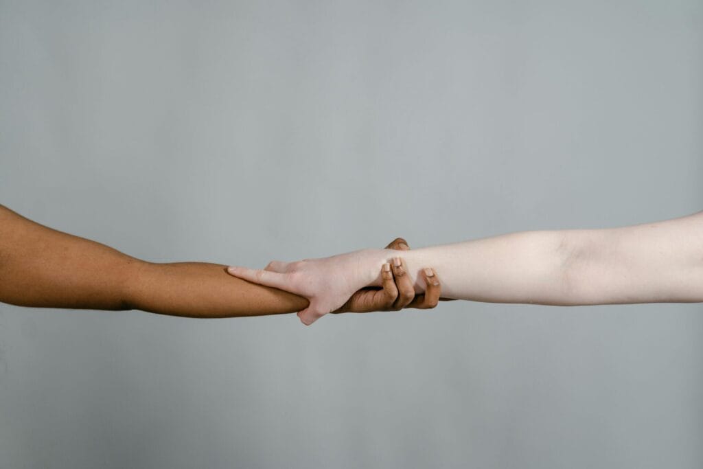 Close-up of two diverse hands reaching towards each other on a plain background, symbolizing unity.
